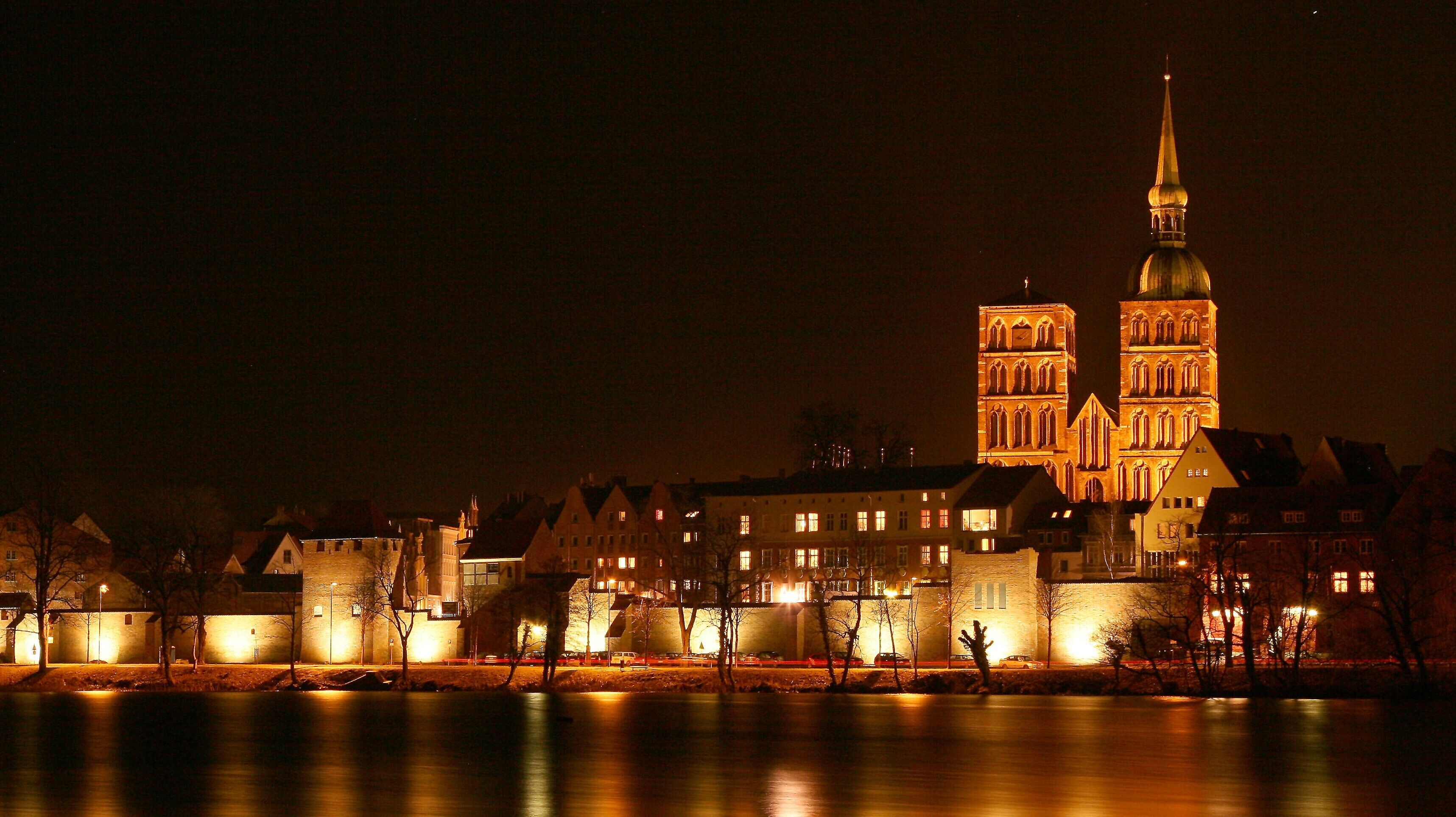 A nighttime view of a historic building with a prominent tower and a spire, surrounded by residential buildings.