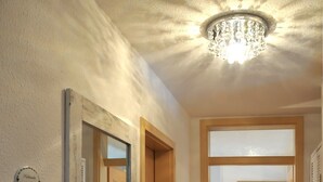 A hallway with wooden flooring, a chandelier, and a door with a mirror and a sign. - Apartment 'Wohnungen 'am Kütertor' - Kogge' with Balcony and Wi-Fi (Stralsund)