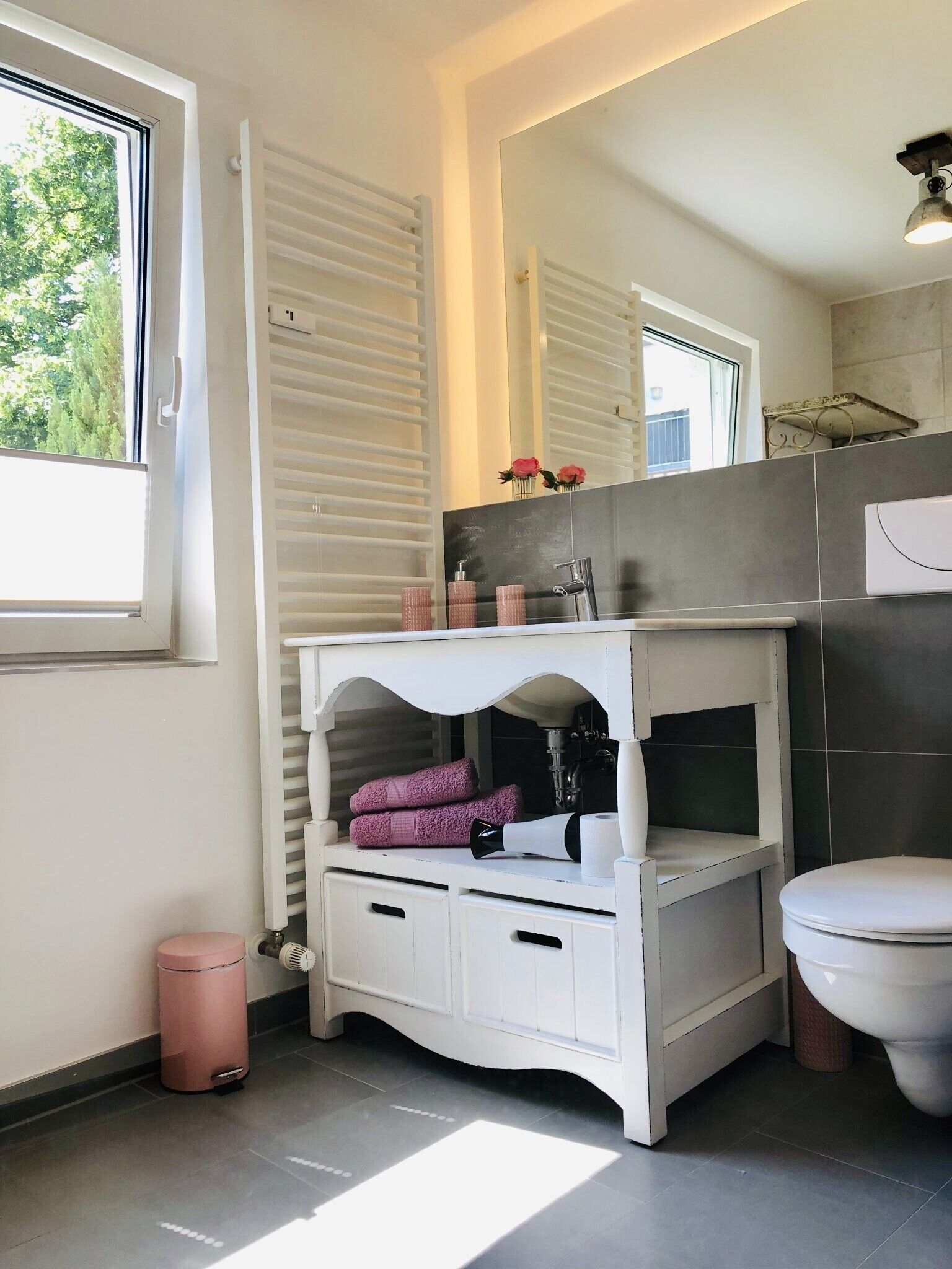 A bathroom with a white vanity, a mirror, a toilet, and a window.