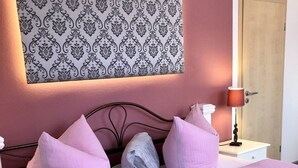 Een bed met roze beddengoed, een wanddecoratie met patroon en een bedlampje.