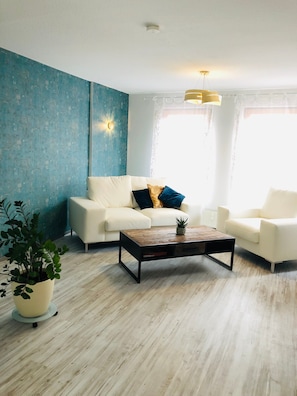 Sala de estar com sofá branco, mesa de centro de madeira e planta em vaso.