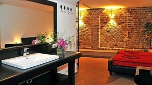 Une salle de bain avec un lavabo blanc, un plan de toilette noir et un miroir. Un vase rempli de fleurs est posé sur le plan de toilette.