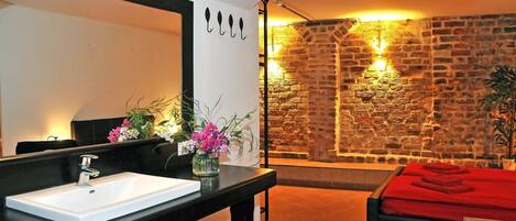A bathroom with a white sink, black countertop, and a mirror. There's a vase with flowers on the countertop.