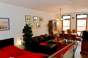 A living room with a sofa, a dining table with chairs, a large plant, and framed pictures on the wall. - Apartment 'Wohnungen 'am Kütertor' - Wikinger' with Private Terrace and Wi-Fi (Stralsund)