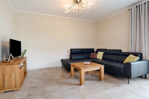 A living room with a sofa, a wooden coffee table, a TV on a wooden cabinet, and a ceiling light fixture.