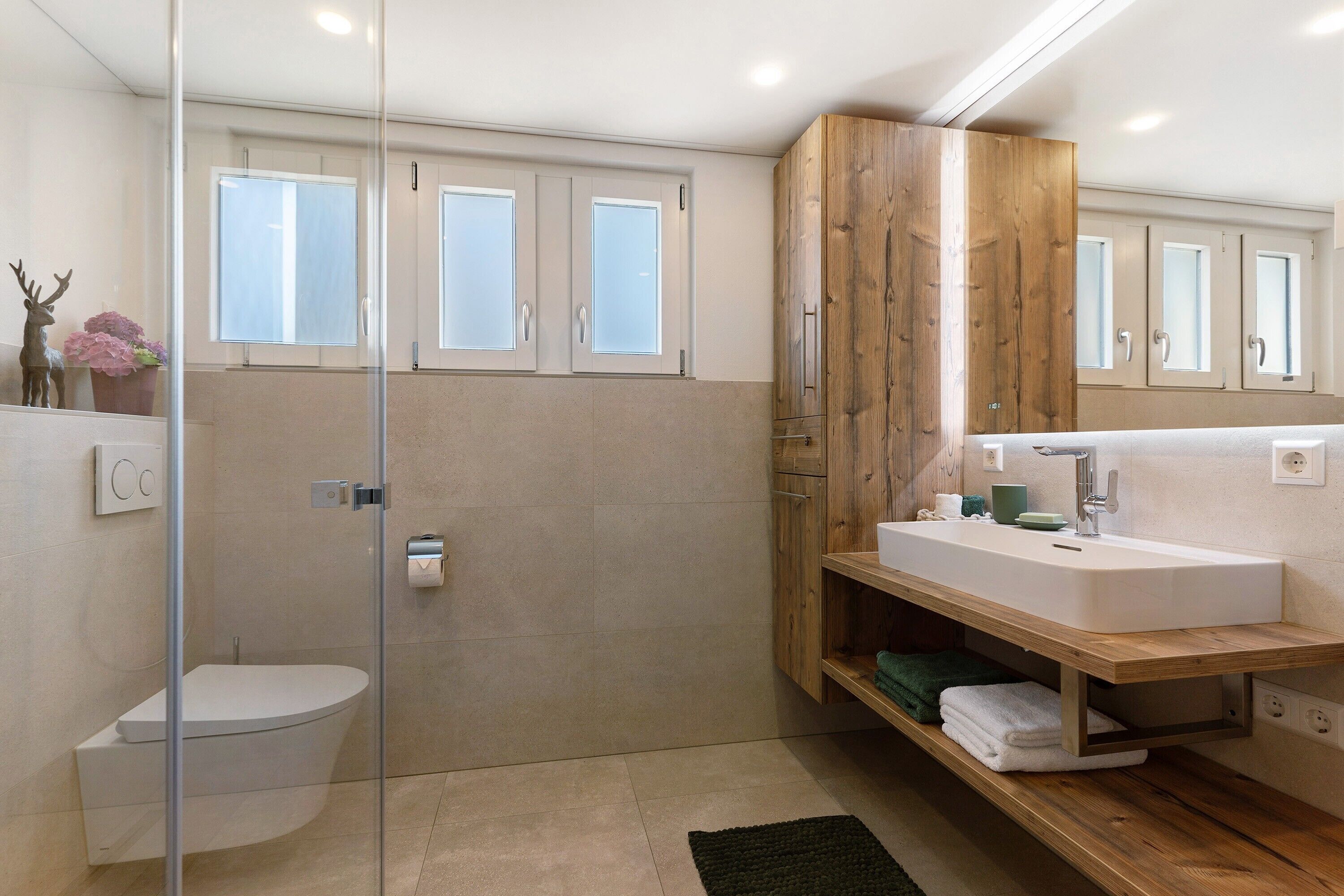 Ein modernes Badezimmer mit Duschkabine aus Glas, Toilette, Holzwaschtisch und Spiegel.