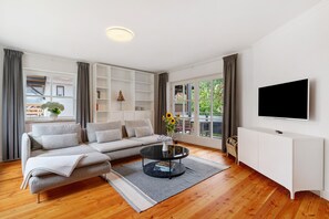 A modern living room with a sofa, a coffee table, a TV, and a bookshelf. - Apartment 'Moderner Schwarzwaldtraum' with Private Terrace, Shared Garden and Wi-Fi (Oberharmersbach)