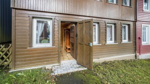 En träbyggnad med en stor, öppen dörr, en liten träbänk inuti och ett inhägnat område.