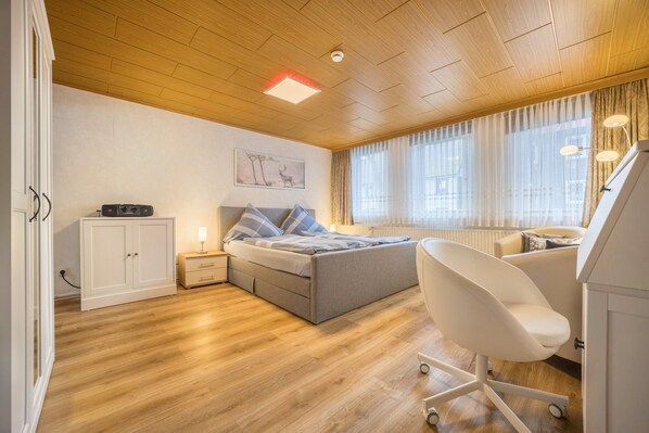 A bedroom with a bed, bedside table, lamp, chair, wardrobe, and a window with curtains.