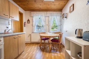 A kitchen with wooden cabinets, a dining table with chairs, a kettle, and a toaster on a shelf.