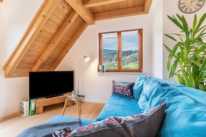 A living room with a television, a sofa, a coffee table, and a large window with a view of the outdoors.