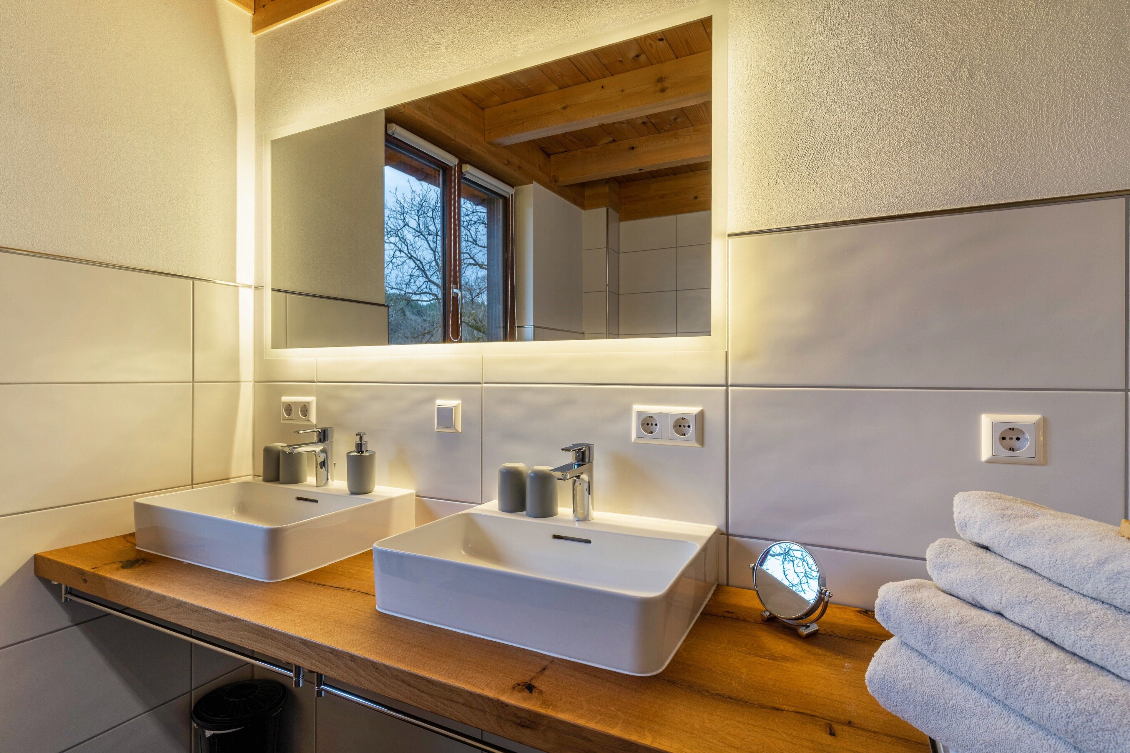 A bathroom with two sinks, a mirror, a window, and towels.
