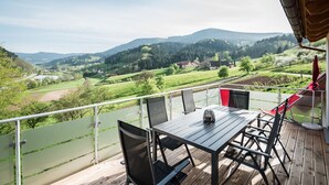 Een balkon met een tafel en stoelen, met uitzicht op een groene vallei met huizen en bomen.
