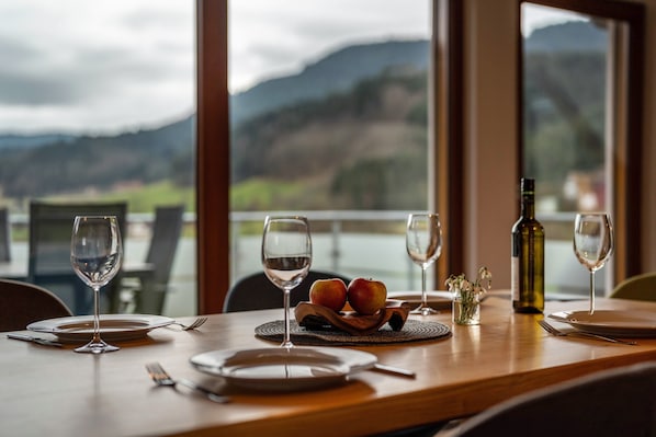 A dining table with wine glasses, plates, cutlery, a bottle of wine, and a bowl of fruit.