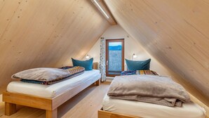 Een knus zolderkamertje met twee houten bedden, een raam met uitzicht en een schuine hemel.