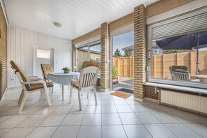 Un patio couvert avec une table et des chaises, donnant sur le jardin arrière, et bordé d’un mur en briques.
