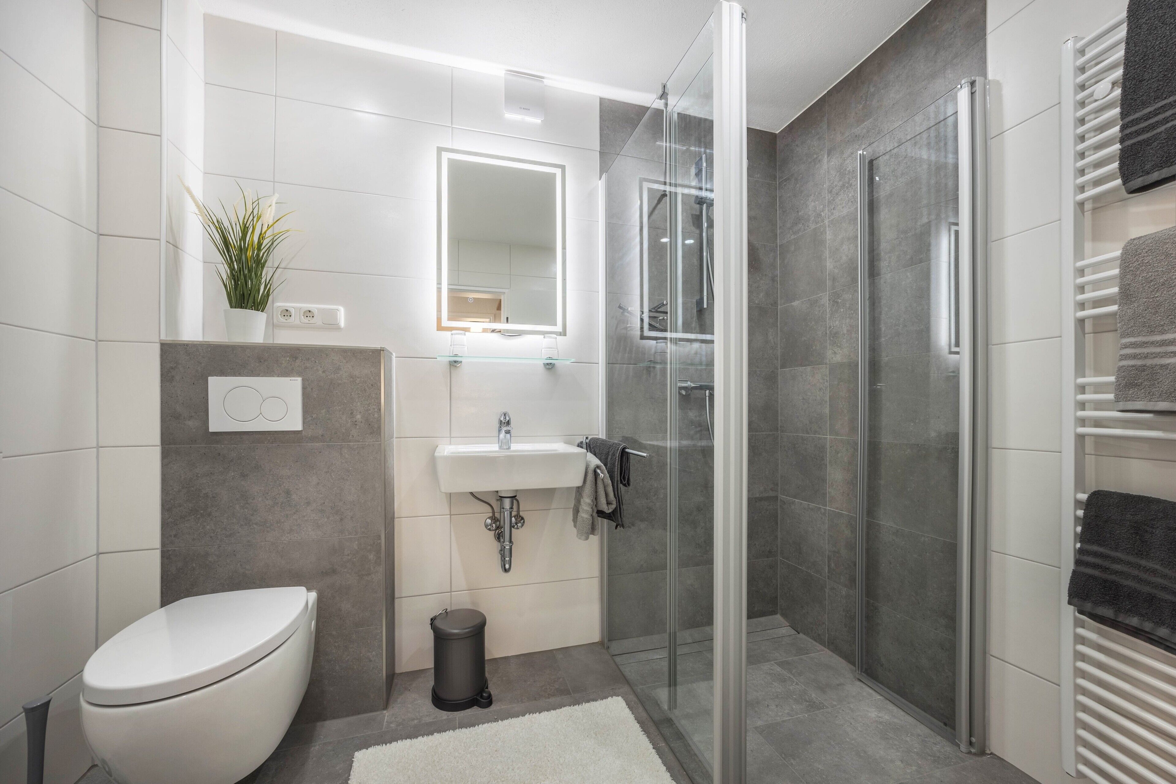 Ein modernes Badezimmer mit Toilette, Waschbecken, Duschkabine aus Glas und einem Handtuchhalter.