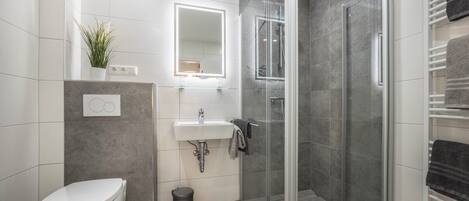 Ein modernes Badezimmer mit Toilette, Waschbecken, Duschkabine aus Glas und einem Handtuchhalter.