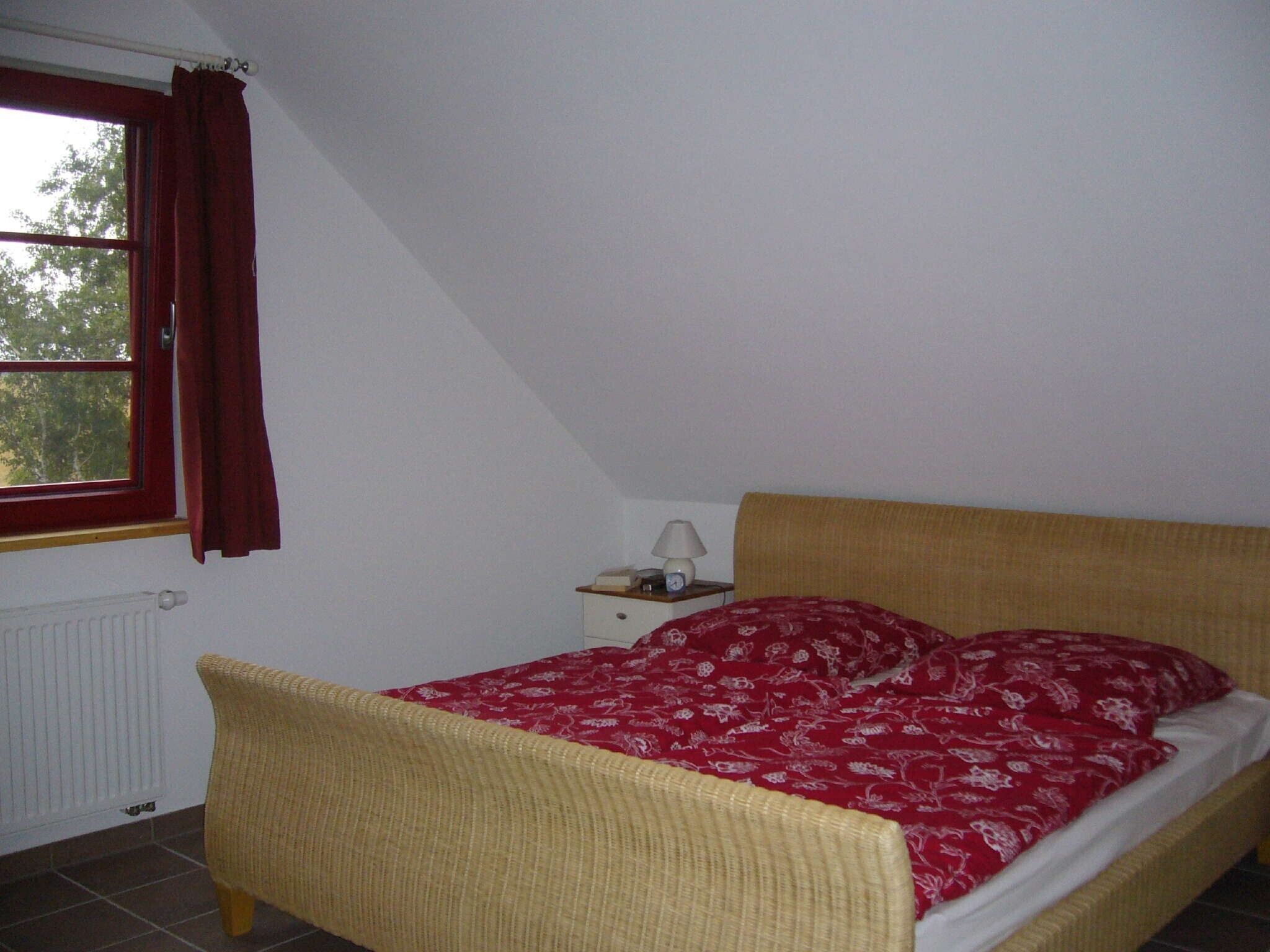 Un dormitorio con cama, mesita de noche, lámpara y ventana con cortinas.