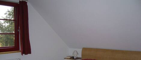 Un dormitorio con cama, mesita de noche, lámpara y ventana con cortinas.