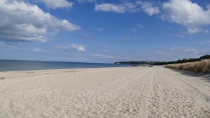 A wide sandy beach with footprints leading to the water, a clear sky, and a distant shoreline with buildings. - Holiday Home 'Sabines Badehaus Mit Innenpool' with Lake View, Private Terrace and Wi-Fi (Breege-Juliusruh)