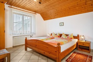 A bedroom with a wooden bed, a nightstand with a lamp, a window with curtains, and a radiator.