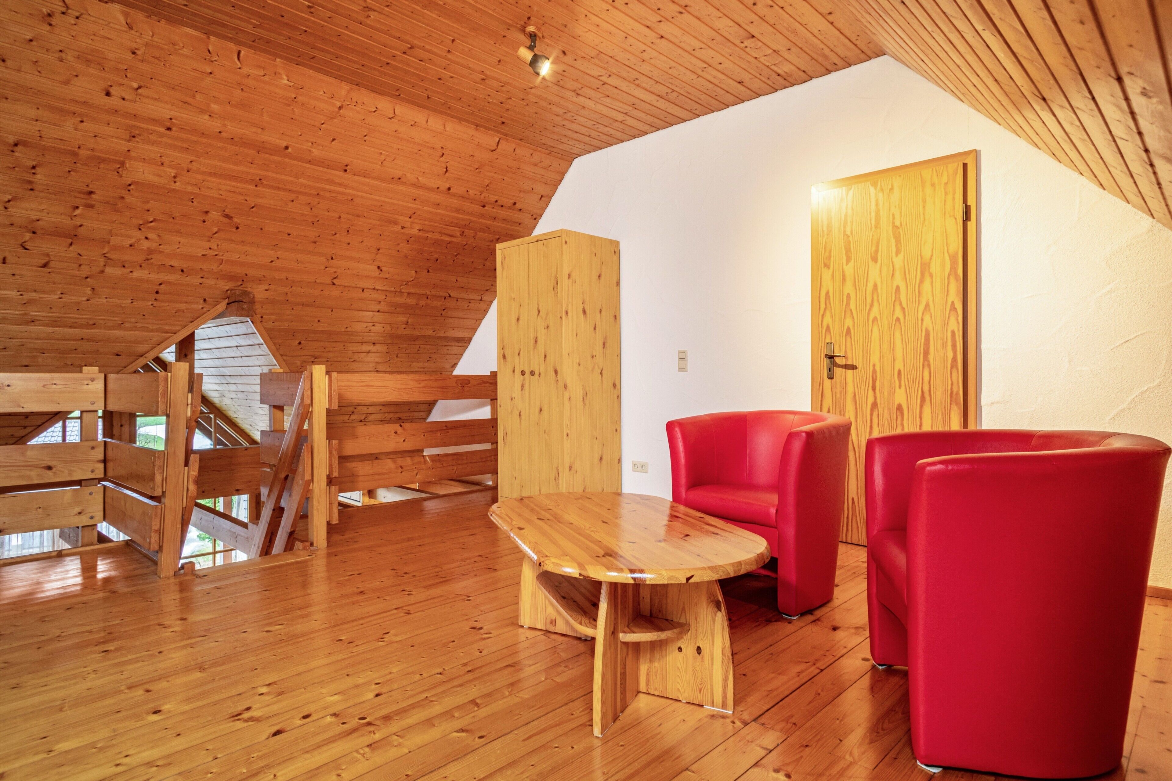 Un intérieur en bois avec une table en bois, des chaises rouges et une porte.
