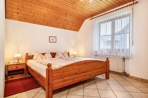 Ein Schlafzimmer mit einem hölzernen Bett, Nachttischen mit Lampen, einem Heizkörper und einem Fenster mit durchsichtigen Vorhängen.