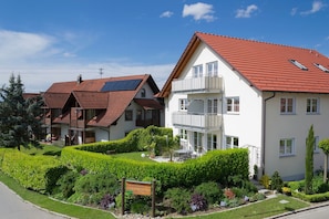 Ein Wohngebäude mit rotem Ziegeldach, einem Balkon und einem gepflegten Garten.