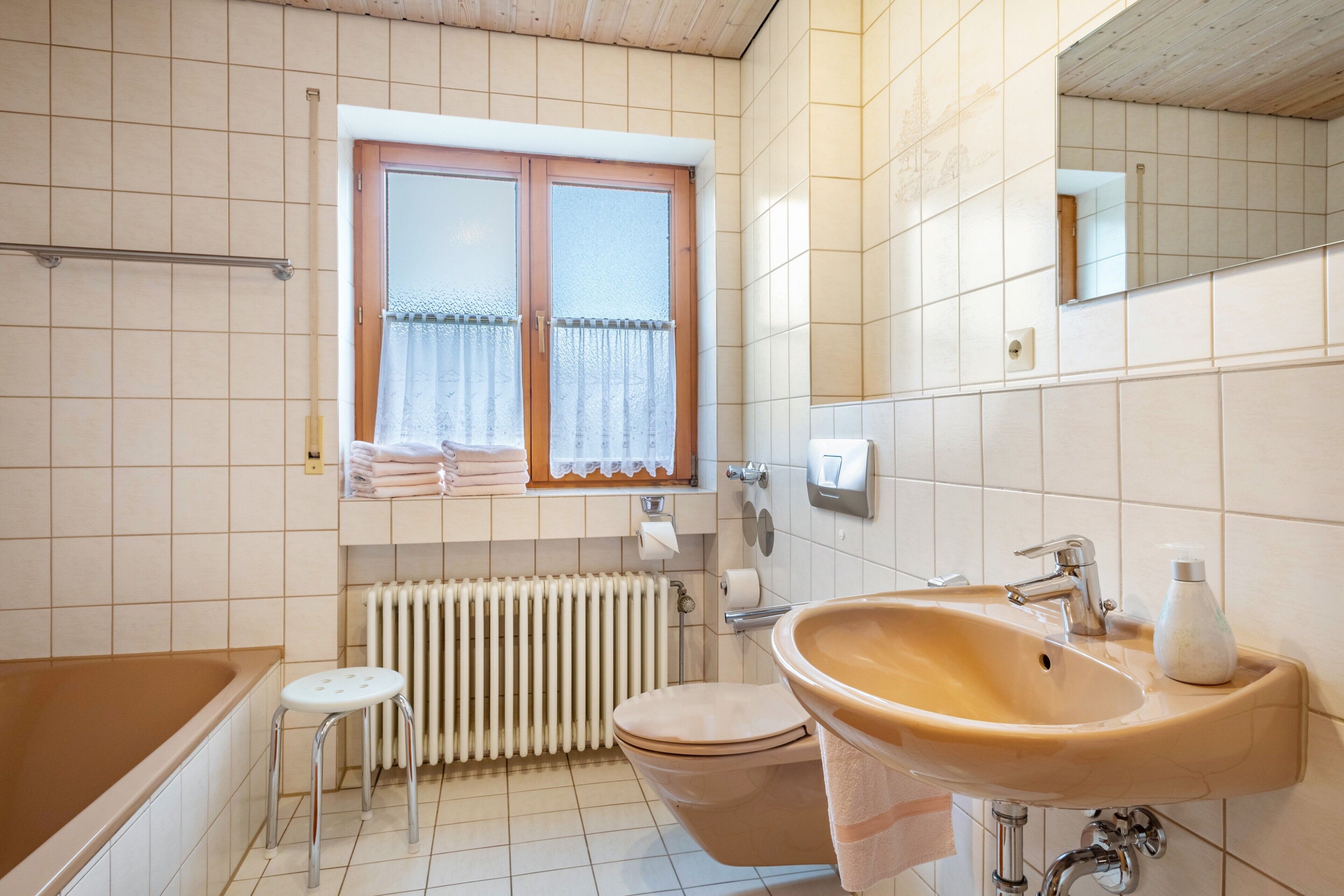 A bathroom with a bathtub, toilet, sink, and window with curtains.