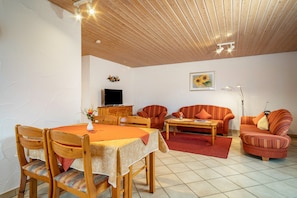 A living room with a dining table, chairs, sofas, a TV, and a lamp.