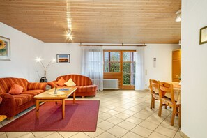 Una sala de estar con un sofá, una mesa de centro, una mesa de comedor con sillas, un radiador y una ventana con cortinas.