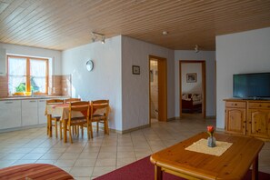 A spacious living area with a wooden dining table, chairs, a television, and a kitchen area with a window. - Apartment 'Ferienwohnung 1, 73qm' with Private Terrace, Shared Garden and Wi-Fi (Kressbronn am Bodensee)
