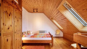 Ein Schlafzimmer im Dachgeschoss mit Holzwandverkleidung, geneigter Decke, einem Bett mit floralem Bettzeug, einem Heizkörper und einem Oberlicht.