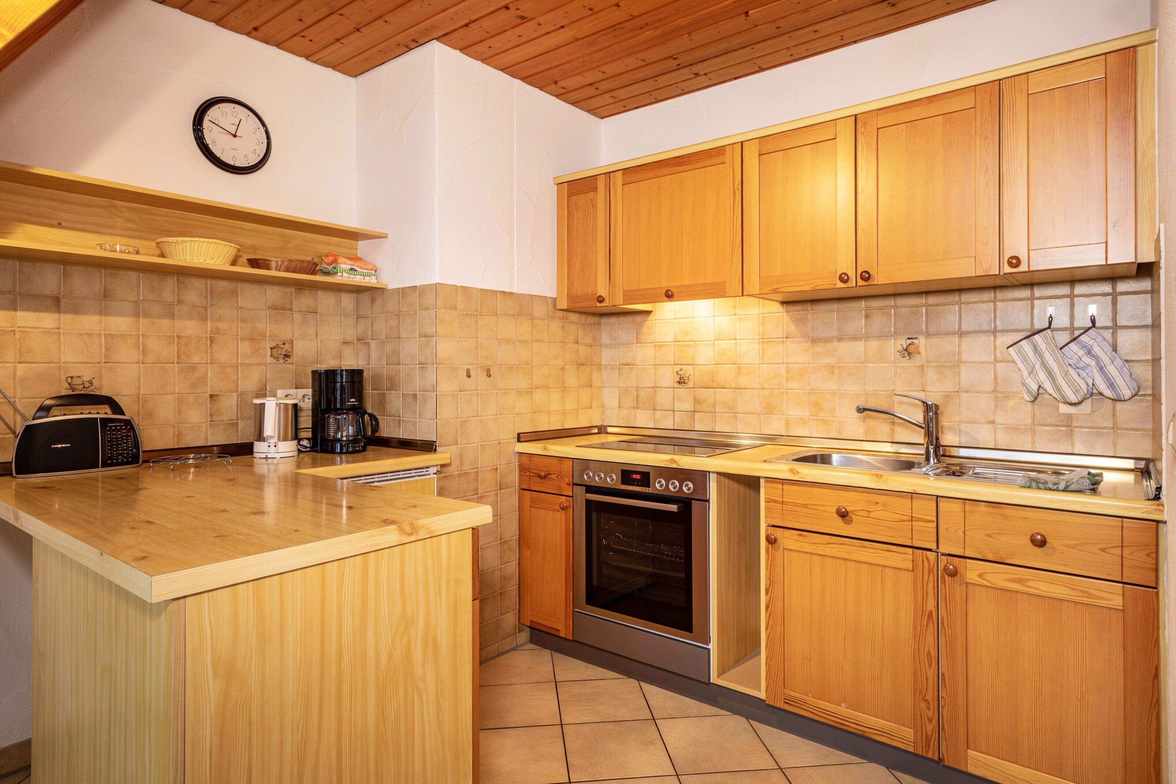 A kitchen with wooden cabinets, a built-in oven, a coffee maker, and a clock on the wall.