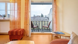 Una habitación con balcón, una mesita, dos sillas, un sofá y una ventana con cortinas.