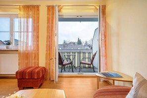 Una stanza con balcone, un tavolino, due sedie, un divano e una finestra con tende.