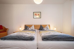 Ein Doppelbett mit Holz Kopfteil, zwei Nachttische mit Lampen, ein Korbstuhl und ein gerahmtes Bild an der Wand.