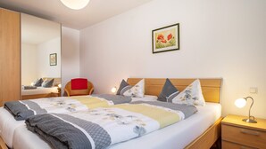 Una cama doble con una colcha estampada, una mesita de noche con lámpara, una mesita auxiliar de madera y un espejo en la pared izquierda.