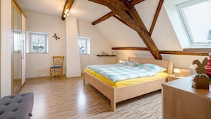 A bedroom with a wooden ceiling, a bed with a blue and yellow bedspread, a chair, a bedside table with a lamp, and a window. - Apartment 'Ferienwohnung Katharina' with Shared Terrace and Wi-Fi (Laufeld)
