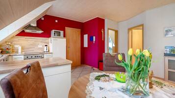 Una cocina moderna con una pared de acento roja, un comedor con una mesa dispuesta para dos personas, y vistas al salón.