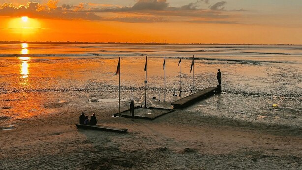 Un atardecer sobre una playa con un muelle y un pequeño bote con gente.