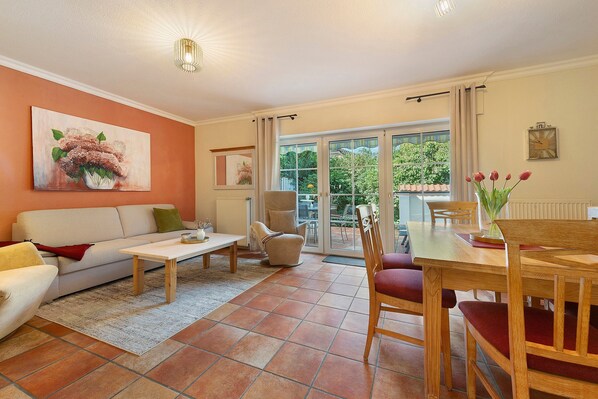 Un salon comprenant un canapé, une table basse et une table à manger avec des chaises. Une porte-fenêtre coulissante donne accès à un patio.