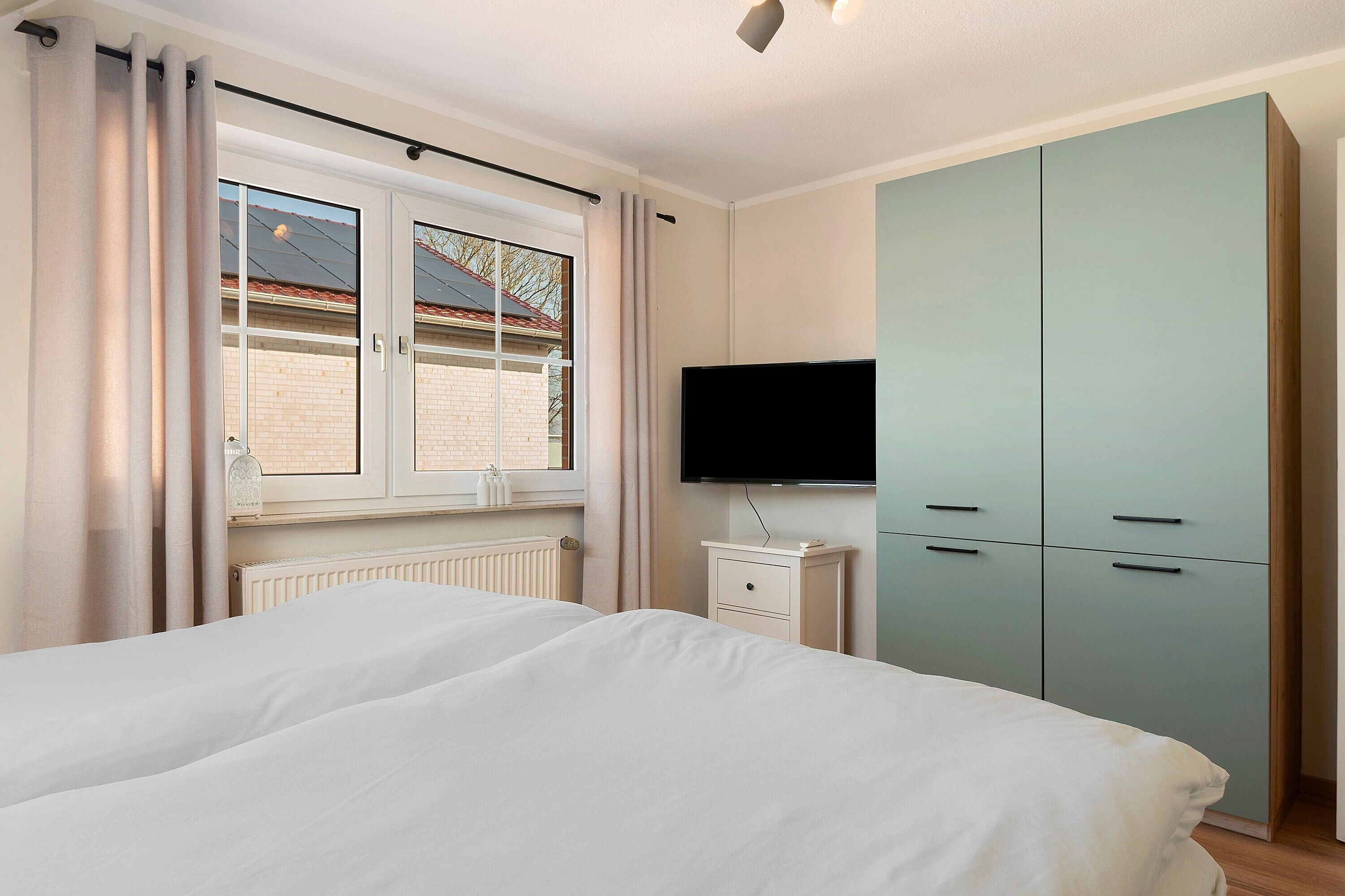 Un dormitorio con cama, televisor, armario y ventana con cortinas.