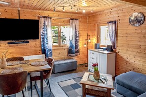 Ein Holzinnenraum mit Fernseher, Esstisch, Stühlen, einer Couch, einer Bank, einem Schrank und einer Uhr.