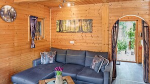 A wooden cabin interior with a sofa, a wall clock, a framed forest picture, and a door leading outside. - Holiday Home Obert - Drognitz with Private Terrace, Garden, Free Boat Use and Wi-Fi (Drognitz)