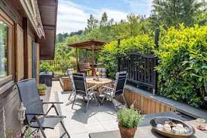 Eine Terrasse mit Tisch und Stühlen, eine hölzerne Pergola und ein Gartenbereich mit Holzzaun und Bepflanzung.