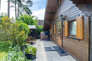 Eine Holzhütte mit Kiesterrasse, einer Holzdar Terrasse und einer Bank.