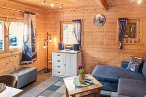 Ein Holzblockhaus-Innenraum mit einer Couch, einem Schrank, einem Tisch mit einer Vase und Vorhängen.