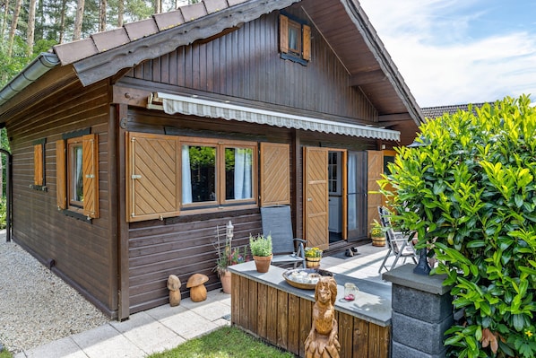 Eine Holzhütte mit Veranda, einer kleinen Sitzgelegenheit im Freien und einem gepflegten Garten.